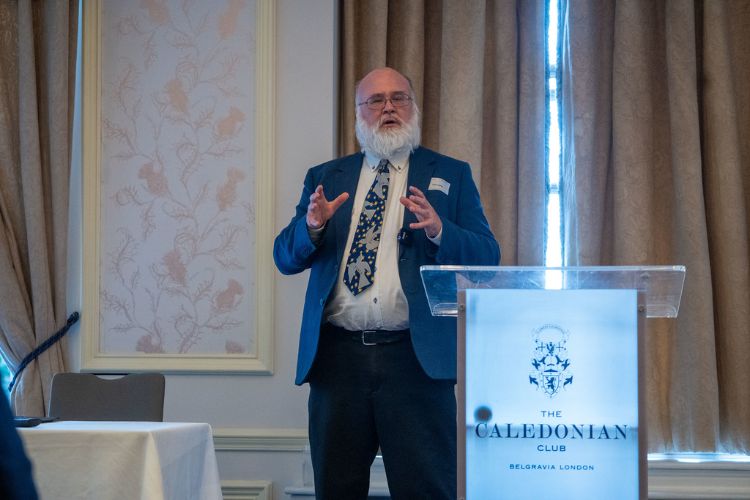 A male academic with a beard in full swing giving a presentation at a lectern